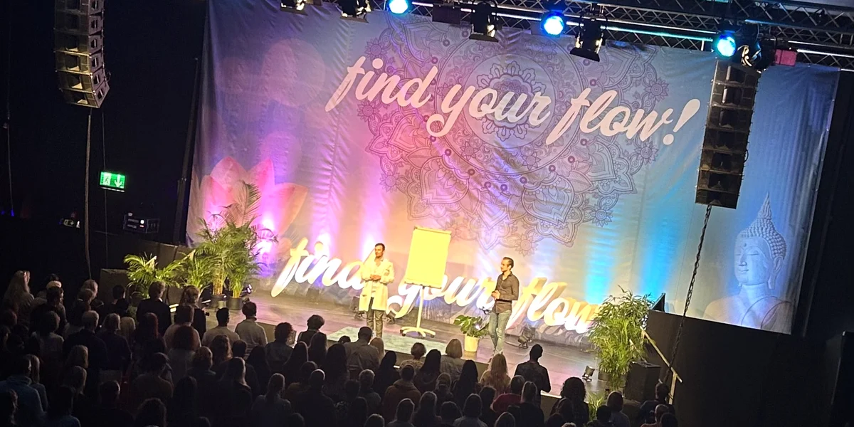 Große Keynote-Veranstaltung beim Find Your Flow Event mit zwei Vortragenden auf der Bühne und zahlreichen Zuschauern.