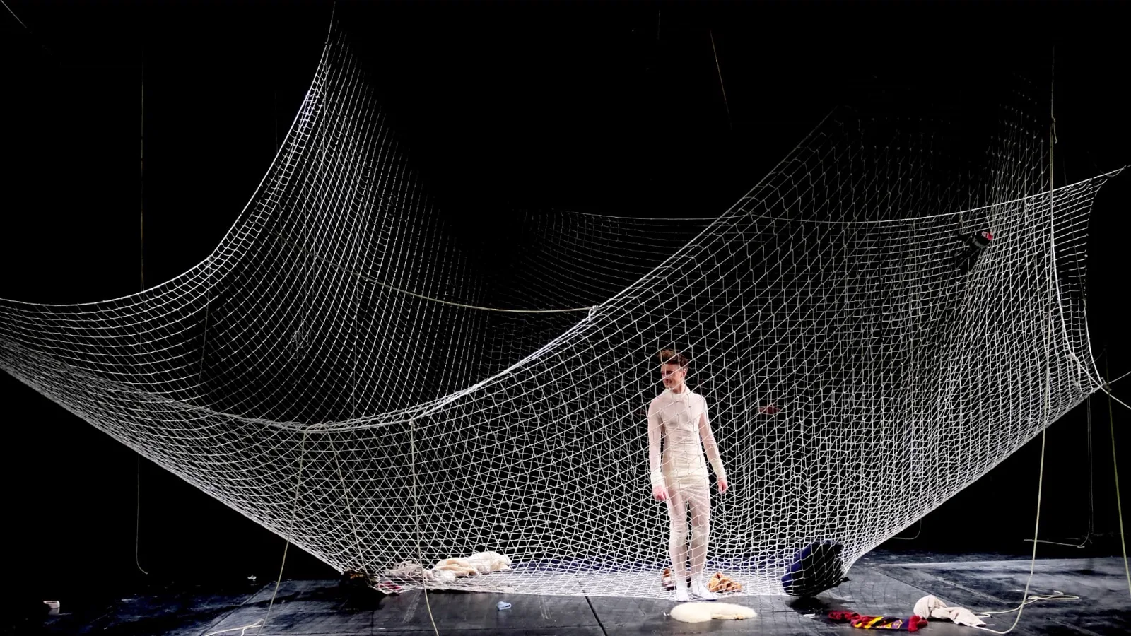 Theaterinszenierung mit weißer Netzinstallation vor schwarzem Bühnenhintergrund